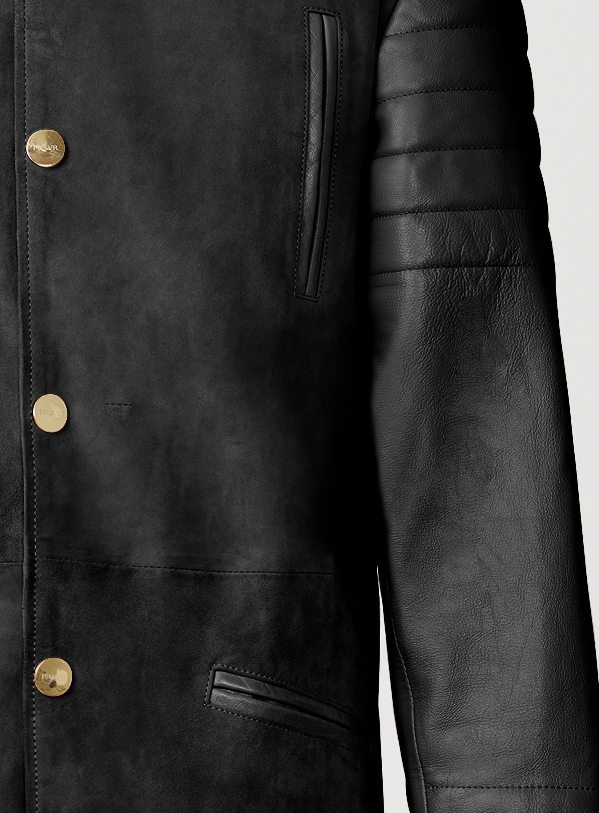 A Beautiful Black Suede Trench Coat, created by designer brand PRSVR. The PRSVR Lab Coat has a suede Body, and lambskin leather sleeves that show off a padded ribbed design on the shoulder and wrist of the sleeve. 